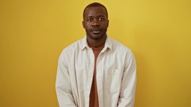 Afro-Amerikalı bir adam, gözleri kapalı bir şekilde dikiliyor. Şaşırtıcı, kör bir jestle, izole edilmiş sarı bir arka planda gülümsüyor.