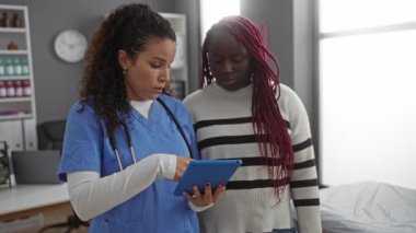 Mavi üniformalı hemşire, hastane odasında tabletle ilgili bilgi gösteriyor.