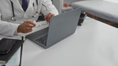 Doktor klinikteki gözlükleri ayarlarken, tıbbi ekipman ve malzemelerle çevrili teletıp konsültasyonu için dizüstü bilgisayar kullanıyor, odak ve profesyonelliği iletiyor.