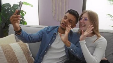 Bir çift, sıcak bir oturma odasındaki kanepede gülüşerek video görüşmesinden zevk alıyor. İçerideki ev bitkilerinin sevgisini ve bağlantısını gösteriyor..