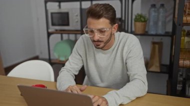 Ofisteki genç adam meditasyon yapmak için bardakları çıkarıyor, rahat bir ifade ve günlük kıyafetle bir masada oturuyor, sakin bir çalışma ortamını kucaklıyor..