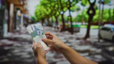 Kentsel bir sokakta Hong Kong doları sayan bir adam, açık şehir ortamında yatırım ve para yönetimi vurguluyor..