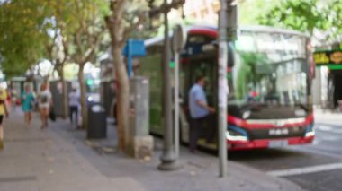 Ağaçlarla kaplı bir sokakta park halindeki bir otobüsün yanında yürüyen insanlar bulanık, odaklanmış ve bokeh arka planda..