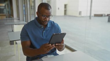 Ofisteki genç adam, modern bir iş yerinde odaklanmış bir ifadeyle tablet kullanıyor.