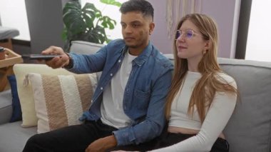 Oturma odasındaki çift televizyon kumandası için şakacı bir şekilde kavga ediyor, neşeli bir an ve modern bir ilişkinin dinamiklerini gösteriyorlar..