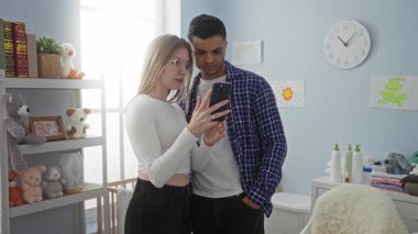 Çift sıcak bir yatak odasında yan yana durur, bebek oyuncaklarıyla çevrili bir telefon ekranına bakar sevgi ve merakla dolu sıcak bir aile ortamı yaratır..