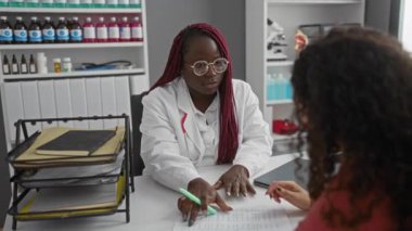 Doktor, iki kadın arasında sağlık hizmetleri etkileşimi olduğunu gösteren tıbbi kayıtları klinikteki hastalarla tartışıyor..