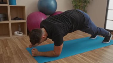 Spor salonundaki mavi bir paspasın üzerinde egzersiz yapan genç bir adam spor yaparken vücut geliştirme, güç ve çekirdeğe odaklanıyor..