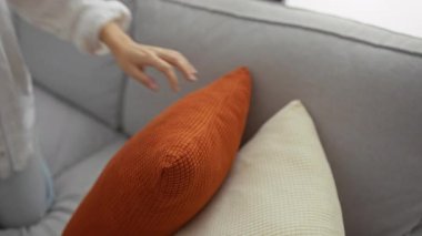 Genç bir kadın rahat bir oturma odasında rahat bir kanepede uzanırken telefonda konuşuyor.