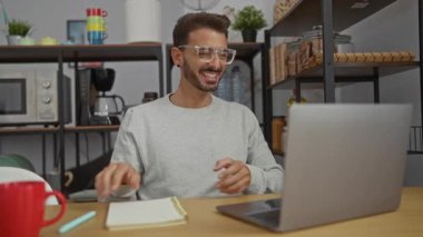 Modern bir ofis ortamında çalışan İspanyol bir adam dizüstü bilgisayar kullanıyor ve not alıyor. Etrafı kapalı bir ortamda organize raflarla çevrili..