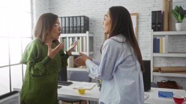 Ofis ortamında, masa başında dokümanlar ve kahve fincanlarıyla tartışan kadınlar büyük pencerenin yanında, modern bir çalışma ortamında iş arkadaşları arasında ciddi bir konuşma yapıldığını gösteriyor.