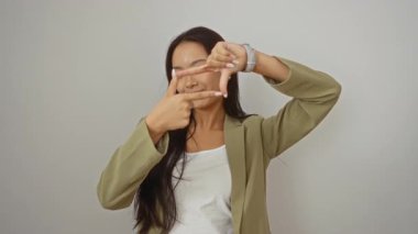 Ceket giymiş genç Çinli bir kadın, beyaz arka planda elleri ve parmakları olan yaratıcı bir çerçeve yapıyor; mutlu, izole edilmiş bir fotoğraf konsepti yüzünü ve hayal gücünü yakalıyor.