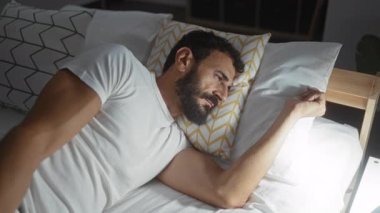 Sakallı genç adam evdeki rahat yatak odasında beyaz çarşaflarla rahat bir şekilde uyuyor.