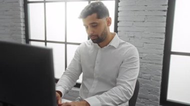 Ofisteki yakışıklı genç adam omzunu acıdan tutuyor. Etrafı geniş pencereli, beyaz tuğladan duvarlı ve masanın üstünde bilgisayar olan modern bir iç mekan ile çevrili..