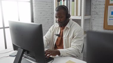 Modern bir ofiste silah çekerken gülümseyen genç bir adam kulaklık ve bilgisayar ile profesyonel çalışma ortamı sergiliyor..