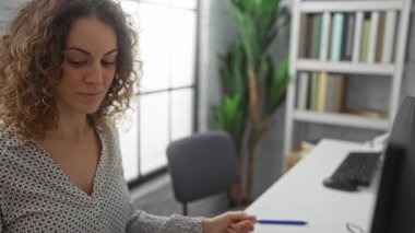 İş yerindeki bir video görüşmesi sırasında gülümseyen bir kadın, profesyonel ofis atmosferini dizüstü bilgisayarla, kitaplıkla ve kapalı alanı geliştiren bitkilerle gösteriyor..