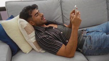 Evdeki kanepede dinlenen, rahat bir oturma odasında akıllı telefon kullanan, sıradan bir yaşam tarzı sergileyen bir adam..