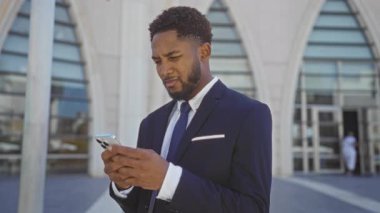 Modern şehir ortamında akıllı telefon kullanan genç adam takım elbise giyiyor.