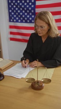 Kadın yargıç, bir Amerikan mahkemesinde belirgin bir şekilde gösterilen bir bayrakla belgeleri imzalıyor..