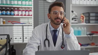 Modern klinik ortamında telefonla konuşan genç bir doktor, steteskoplu laboratuvar önlüğü giyiyor, tıbbi şişe ve malzemelerle çevrili, profesyonel sağlık hizmetleri ortamı sergiliyor..