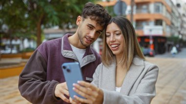 Şehir caddesinde akıllı telefonlara bakarken kadın ve erkek gülümsüyor..