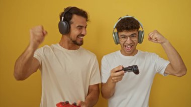 Baba ve oğul neşeli bir anı paylaşıyorlar. Canlı sarı bir arka plana karşı video oyunları oynuyorlar. Aile sevgisini ve yakınlaşmayı gösteriyorlar.