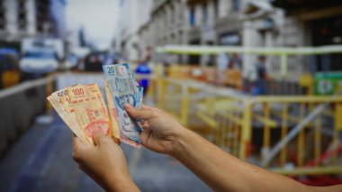 Şehrin işlek bir caddesinde iş ve yatırım temalarını ima eden kentsel inşaat geçmişine sahip Meksika pesolarını tutan eller..