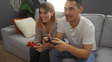 Kadın ve erkek rahat bir oturma odasında video oyunu oynuyorlar, eğlenceli bir çifti evde eğlendiriyorlar, güçlü bir ilişkiyi vurguluyorlar ve hobilerini paylaşıyorlar..