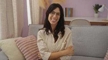 Modern bir oturma odasında rahat bir atmosferi olan rahat bir koltukta oturmuş gülümseyen genç kadın.