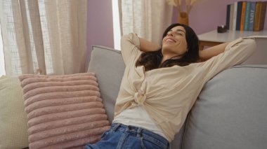 Genç bir kadın rahat bir oturma odasında, rahat ve mutlu görünüyor..