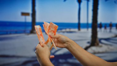Filipin pesolarını sayan bir adam deniz kenarında finans ve seyahat temalarını canlı yaz aylarında banknotlarla sergiliyor, iş ve yatırım potansiyelini yansıtıyor..