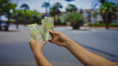 Şehir sokaklarında Şili pesolarını elinde tutan adam, açık hava ticaret odaklı bir şehir ortamında yatırım ve finansal konseptler sergiliyor..