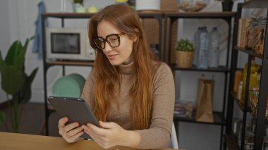 Kapalı ofis ortamında çalışan, elinde tablet ve gözlük tutan, modern ofis dekorlarıyla çevrili profesyonel bir çevrede raflar ve bitkiler olan bir kadın..