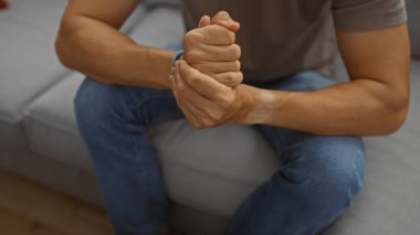 Genç İspanyol bir adam evde oturmuş, rahat bir oturma odasında el ele tutuşuyor, gündelik bir apartman dairesinde tefekkür ya da endişeyi dile getiriyor..