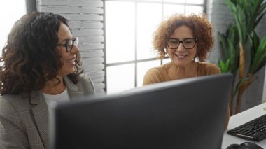 Büyük pencerelerden gelen doğal ışıkla, takım çalışması, pozitiflik ve modern profesyonel bir ortamda iş birliği yapan kadınlar..