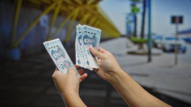 Bir şehir caddesinde Çin Yuan banknotları tutan adam, kalabalık bir şehir ortamında açık hava mali işlemleri veya döviz takasını öneriyor..