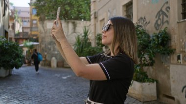 Güneşli bir günde Roma 'da şehrin manzaralı eski caddesini akıllı telefonla çeken kadın şehir cazibesini ve İtalyan mimarisini yakalıyor..