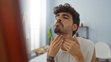 Yakışıklı, sakallı, sağlıklı bir spa salonunda yüzüne dokunan genç bir adam.