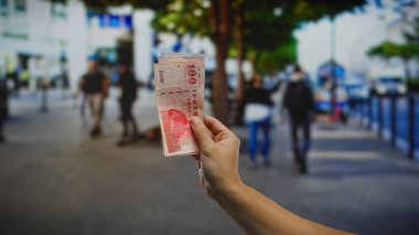 Kentsel sokak düzenlemelerinde el ele tutuşan Tayvan banknotları, bulanık yayaların bulunduğu kalabalık bir açık şehir ortamında finans, yatırım ve iş kavramını resmediyor.