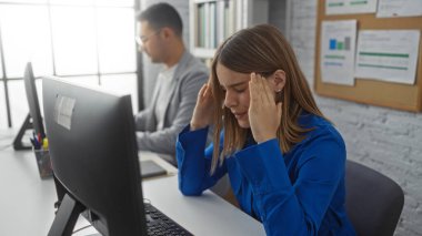 Kadın, arka planda bilgisayarın başında çalışan bir adamla, modern iş yerlerindeki çeşitli çalışanlarla iş ortamını göstererek, kapalı alanda baskı altında,.