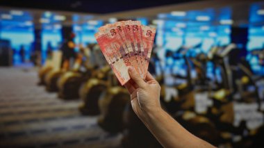 Güney Afrika Rand banknotları kapalı bir spor salonunda el ele tutuşuyor, finans ve fitness entegrasyonuna odaklanarak iş ve para değişimi temalarını resmediyor.