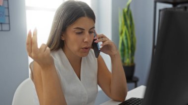 Ofiste telefonla konuşan genç bir kadın profesyonel ve odaklanmış bir çevreyi gösteren bir bilgisayar üzerinde çalışıyor.