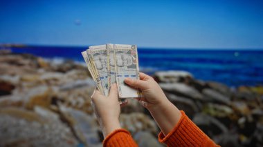 Kadın, deniz kenarı zemininde Peru tabanı tutuyor. Manzaralı bir sahil manzarasına karşı döviz vurguluyor. Açık havada finansmanı boş zamanlarla harmanlıyor..