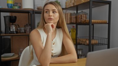 Ofis ortamında raflar ve mutfak malzemeleriyle gezen, kolsuz bir bluz giyen, sakin ve düşünceli bir ruh hali sergileyen bir kadın..