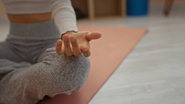Evde yoga yapan bir kadın spor salonundaki paspasın üzerinde meditasyon pozisyonu gösteriyor.