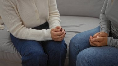 Oturma odasında kanepede oturan kadınlar aile bağlarını ve aile sevgisini kapalı mekanlarda bir araya getirerek samimi bir anne kızı anını yakalıyorlar..