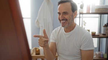 Kuaförde aynaya bakan İspanyol bir adam. İçi rahat bir sağlık merkezinde güvenle gülümsüyor. Olgun ve yakışıklı bir görünümü yansıtıyor..