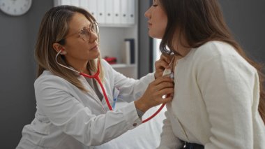 Hastane kliniğinde steteskopla hasta kadını muayene eden, profesyonel bir ortamda tıbbi bakım sergileyen, sağlık uzmanlığı ve ilgi gösteren bir doktor..