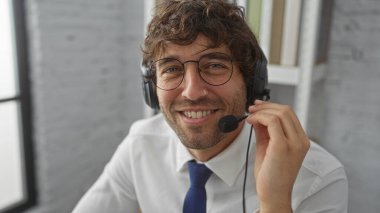 Ofiste gülümseyen, kulaklık takan, iletişim kuran, modern bir iş ortamında profesyonel ve dostane bir tavır sergileyen bir adam..