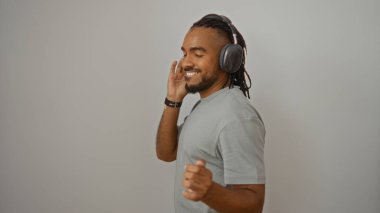 Yakışıklı adam kulaklıkla neşeyle dans ediyor, izole edilmiş beyaz bir arka plana karşı mutluluğu ifade ediyor, şık bir görünüm ve kendine güvenen bir enerji sergiliyor..